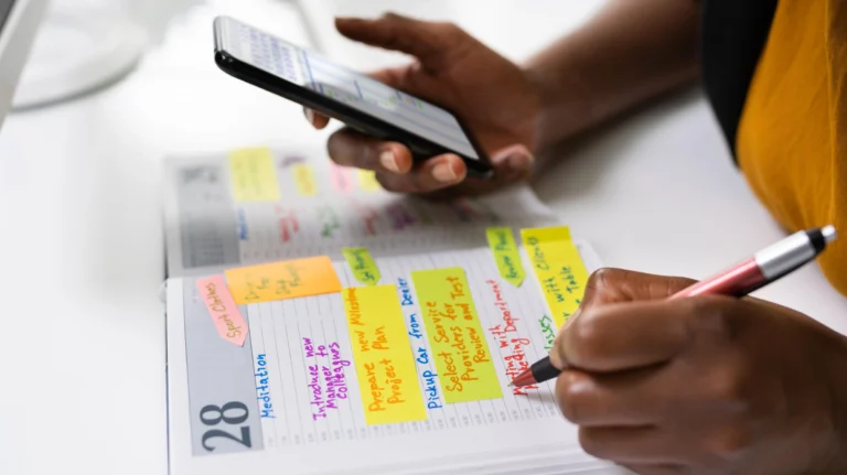 Person writing in a color coded planner while referencing a smartphone schedule
