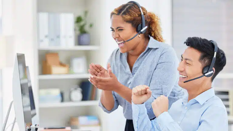 Two cheerful customer service agents wearing headsets celebrating a positive interaction while working at a desk highlighting excellent customer experience