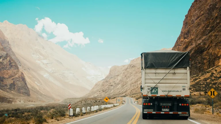 Cargo truck driving on a winding mountain road under a clear blue sky