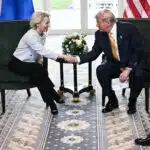 Donald trump and ursula von der leyen shake hands after concluding a u S  eu agreement flanked by american and eu flags