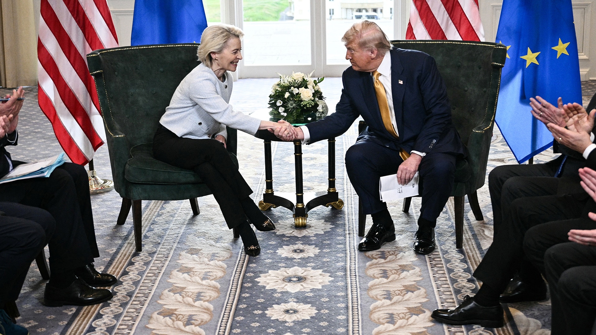 Donald trump and ursula von der leyen shake hands after concluding a u S  eu agreement flanked by american and eu flags
