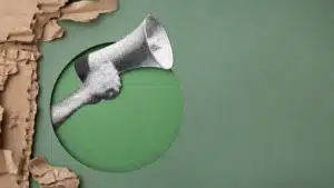 Hand holding a megaphone through torn paper on a textured green background