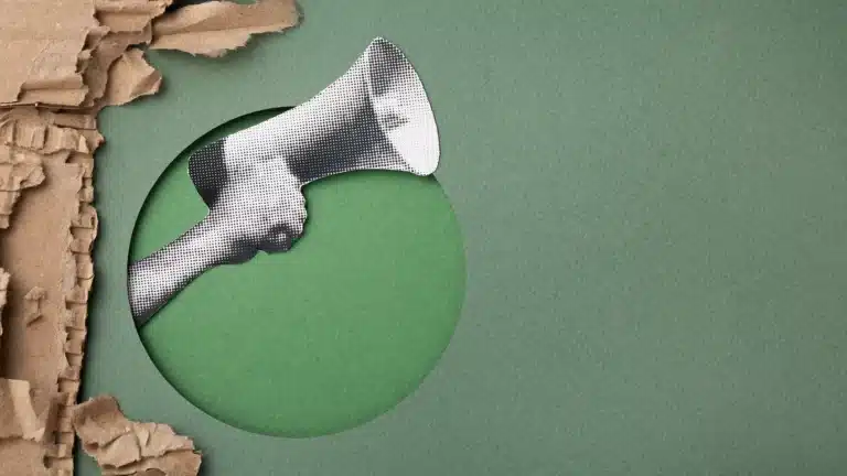 Hand holding a megaphone through torn paper on a textured green background