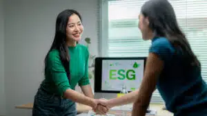 Two women shaking hands in front of a computer displaying esg graphics
