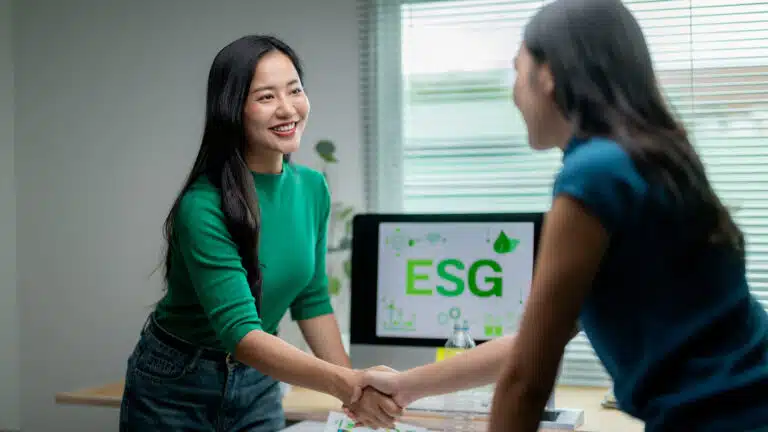 Two women shaking hands in front of a computer displaying esg graphics