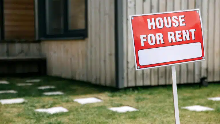 Close up of a house for rent sign in front of a wooden home