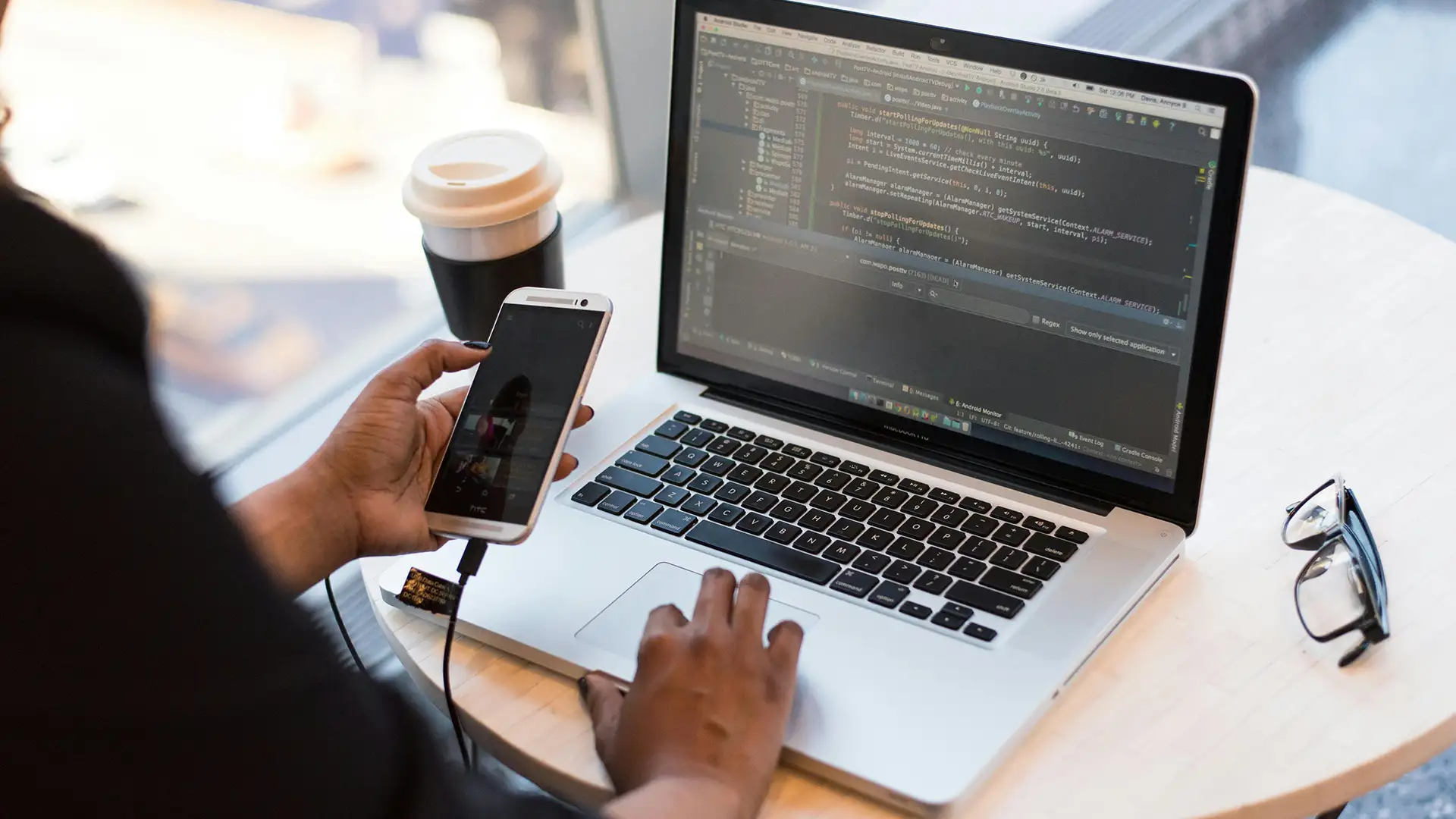 Close up of a developer coding erp software on a laptop while holding a smartphone emphasizing mobile integrated development
