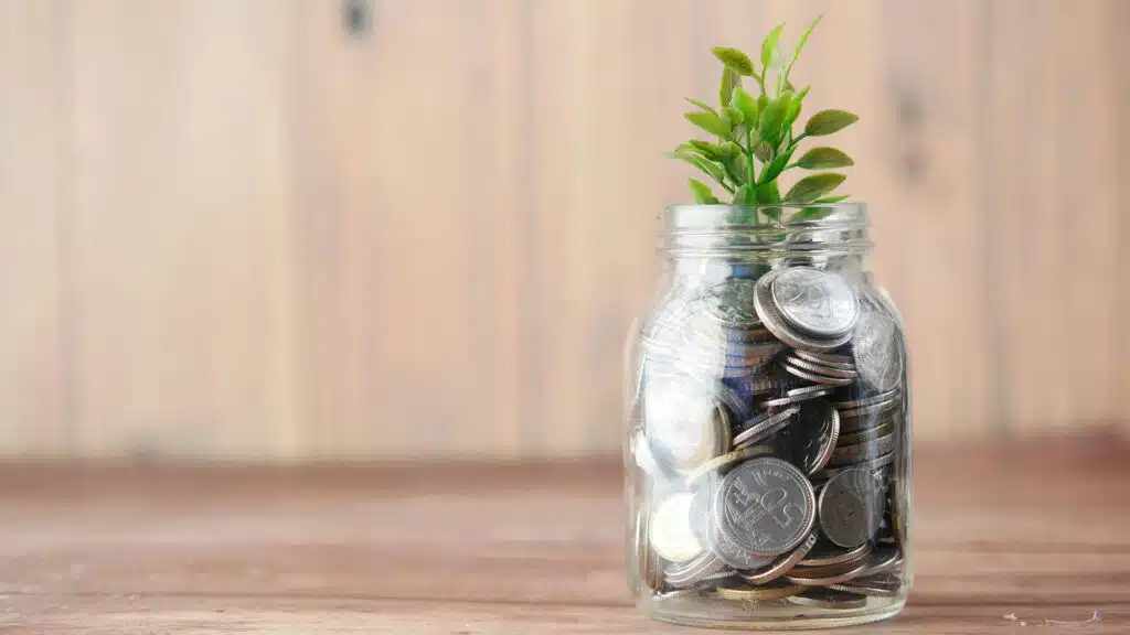 Jar filled with coins and a green plant growing from it symbolizing financial growth