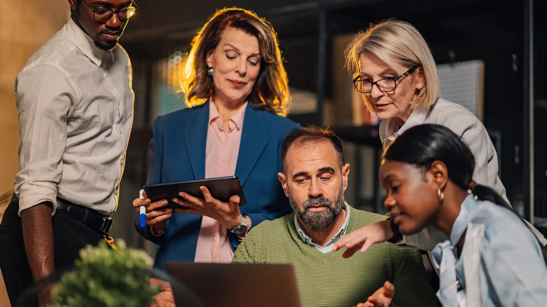 A diverse team of professionals gathered around a laptop in a modern office collaborating on a project