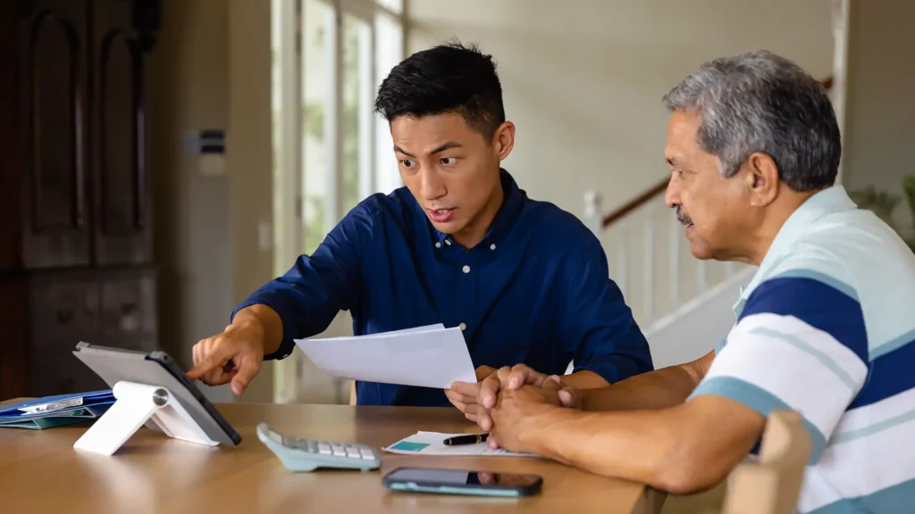 Young man helping senior man review documents and apply for a personal loan using a tablet in singapore