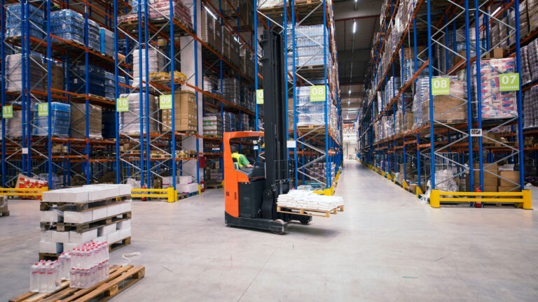 Forklift operator moving pallets inside a high-rack industrial warehouse.