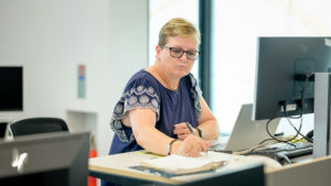 Woman working at computer desk while reviewing handwritten notes