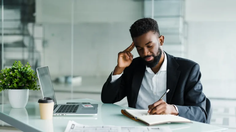 Young african entrepreneur writing notes in an office with a laptop and coffee cup