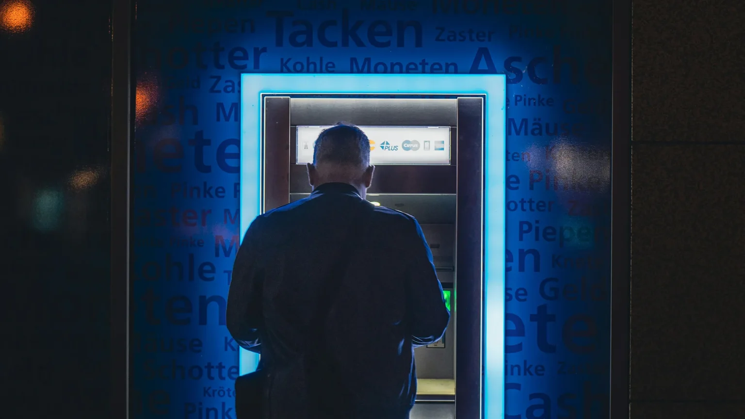 Man using atm at night with glowing blue light