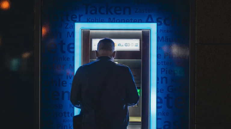 Man using ATM at night with glowing blue light