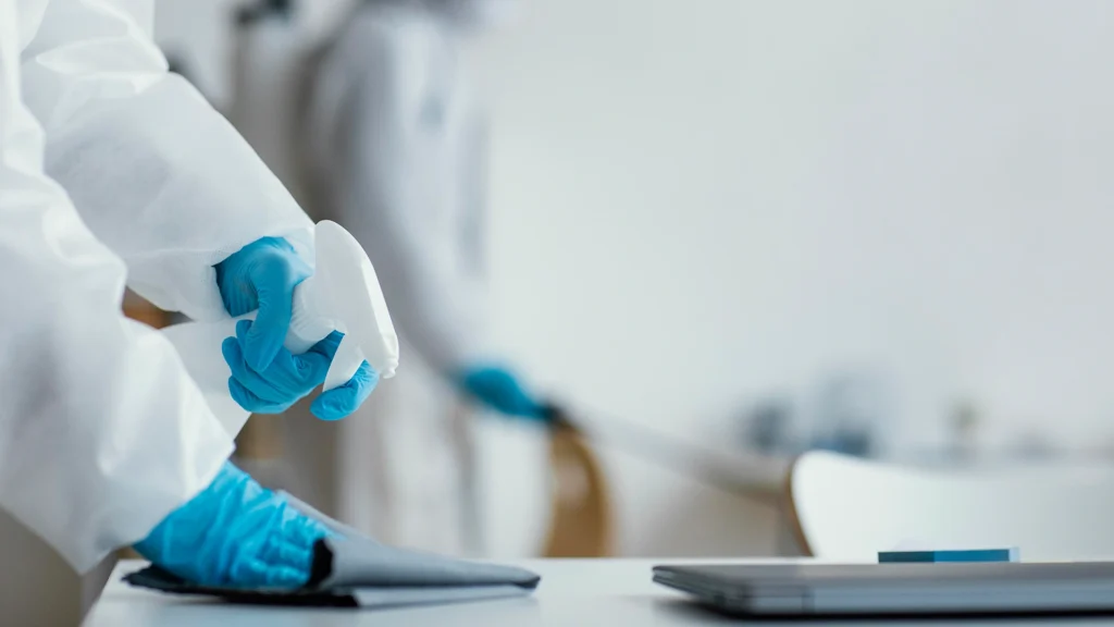 Worker in protective gear sanitizing a surface with a spray bottle