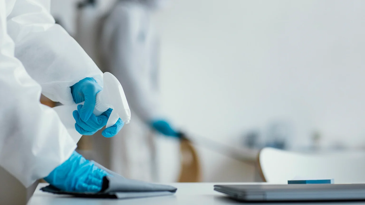 Worker in protective gear sanitizing a surface with a spray bottle