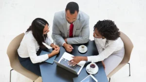 Three business professionals in a meeting discussing strategy with a laptop and coffee