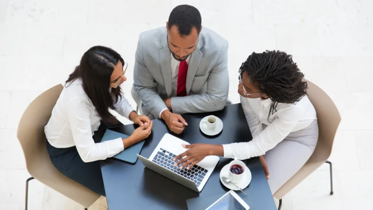 Three business professionals in a meeting discussing strategy with a laptop and coffee