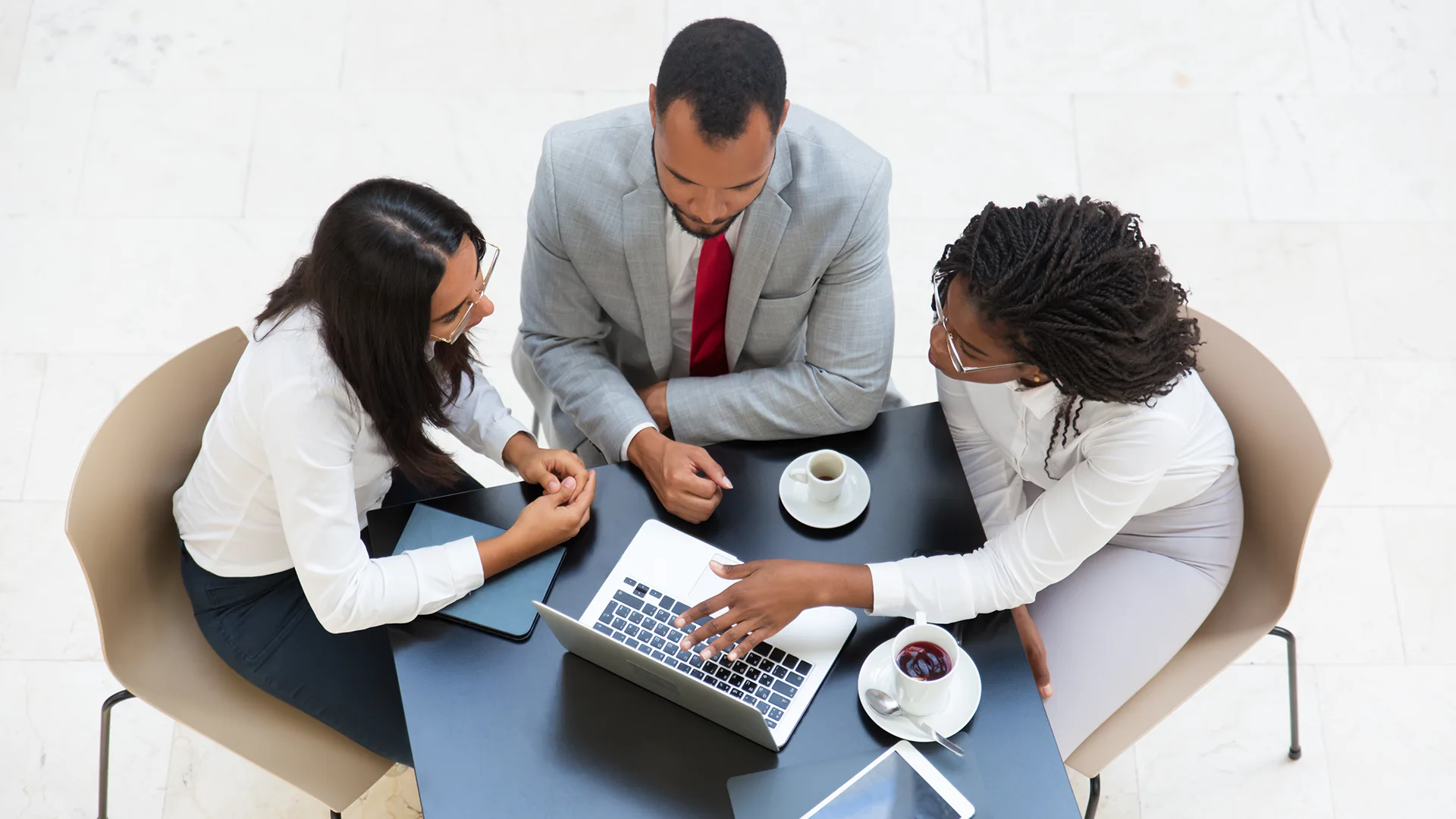 Three business professionals in a meeting discussing strategy with a laptop and coffee