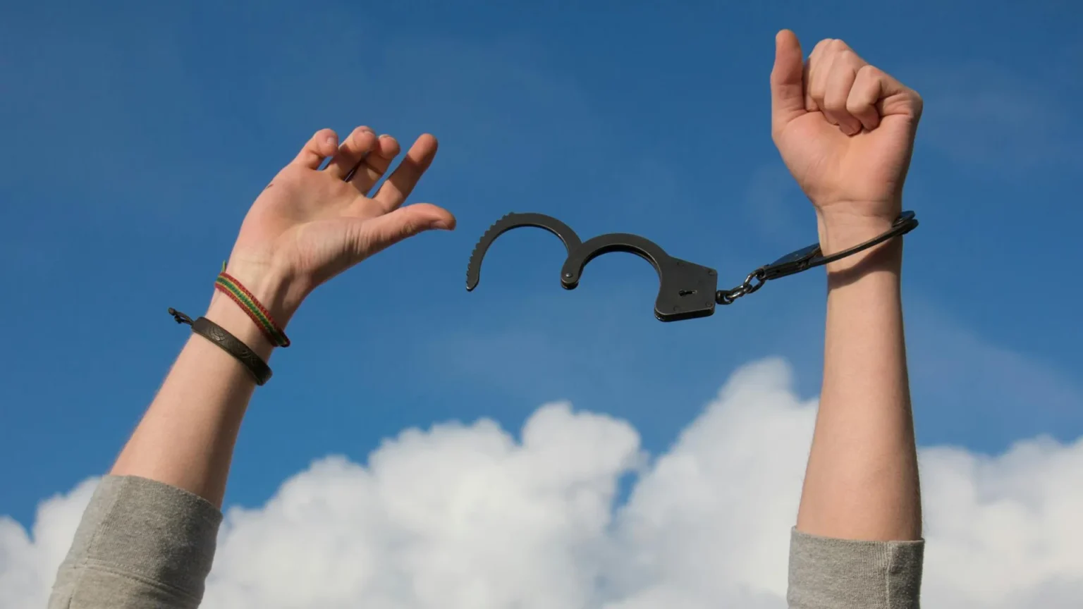 Hands breaking free from handcuffs under blue sky symbolizing financial freedom