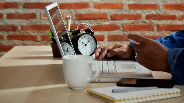 Person using laptop with notebook, coffee, and clock on desk, illustrating time blocking productivity method.