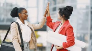 Two professional women high fiving after achieving a workplace milestone