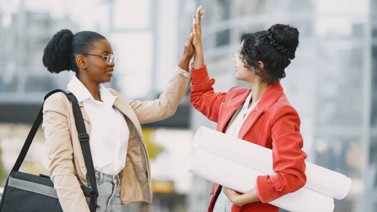 Two professional women high-fiving after achieving a workplace milestone.