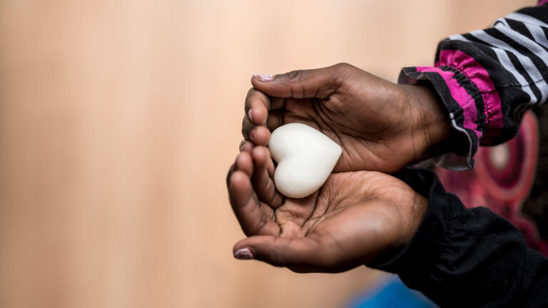 Closeup of childs hands holding a heart shaped marble stone symbolizing love and compassion