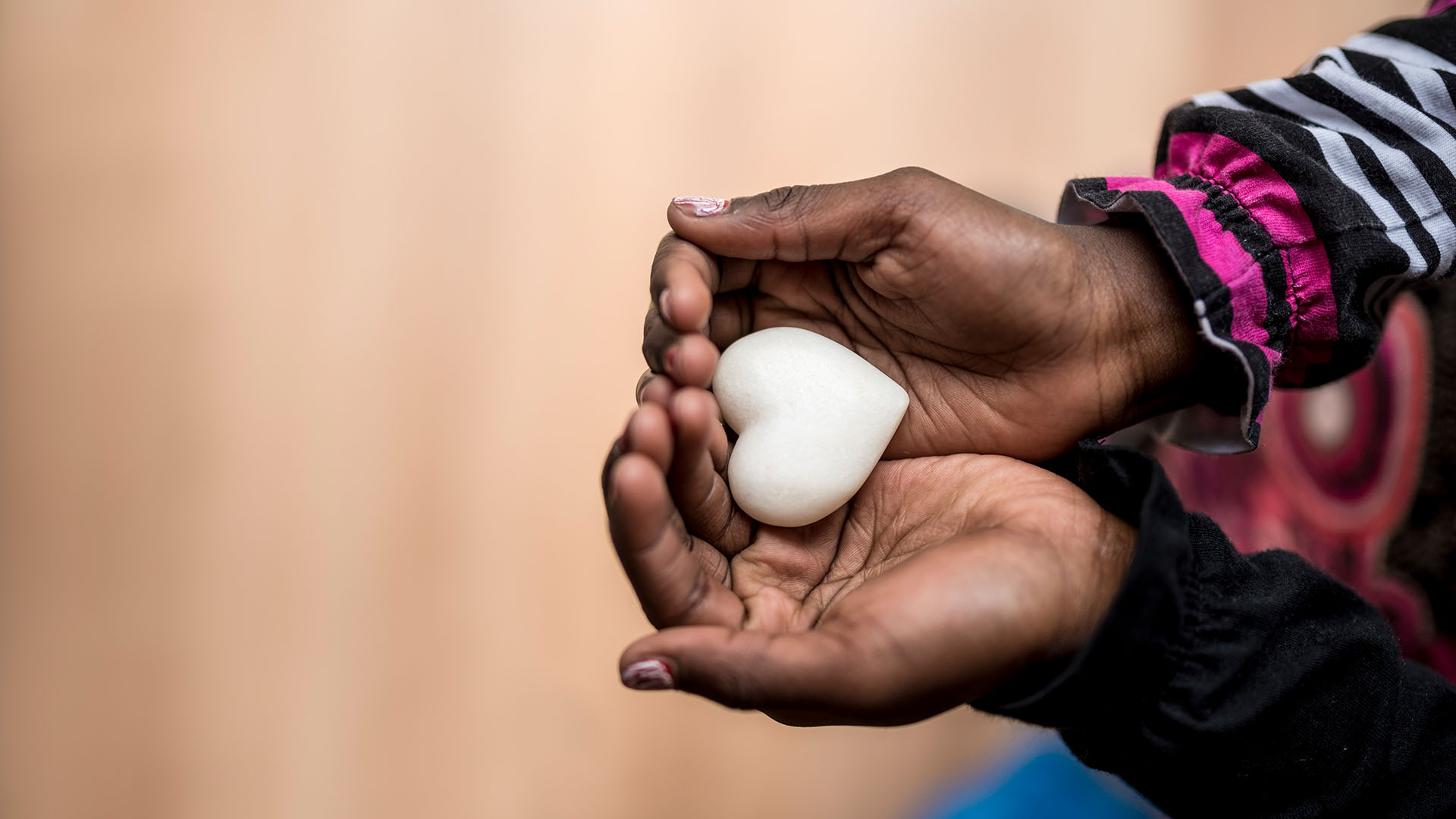 Closeup of childs hands holding a heart shaped marble stone symbolizing love and compassion