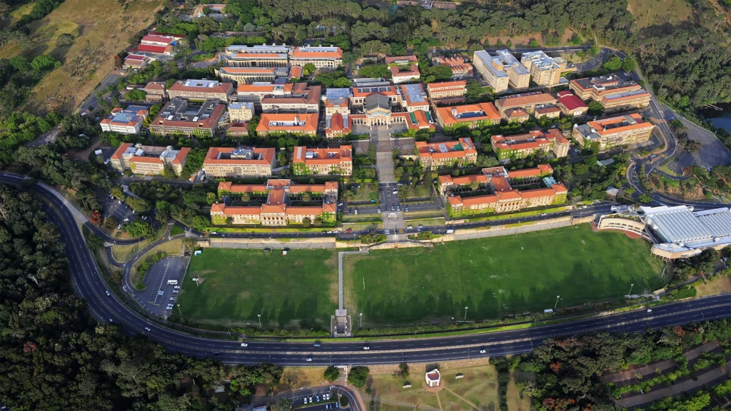 Aerial photograph of the university of cape towns upper campus with red roofed buildings surrounded by greenery and sports fields below