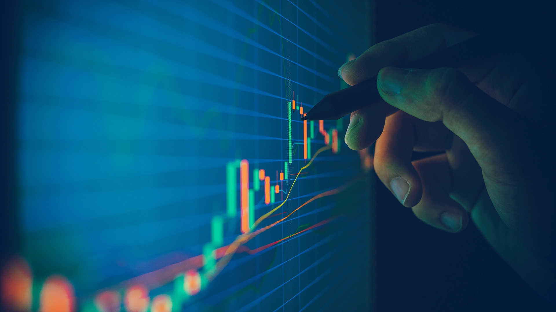 Close up of a hand using a stylus on a digital screen showing stock market data and candlestick charts