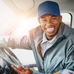 Smiling driver holding a tablet inside vehicle cabin.