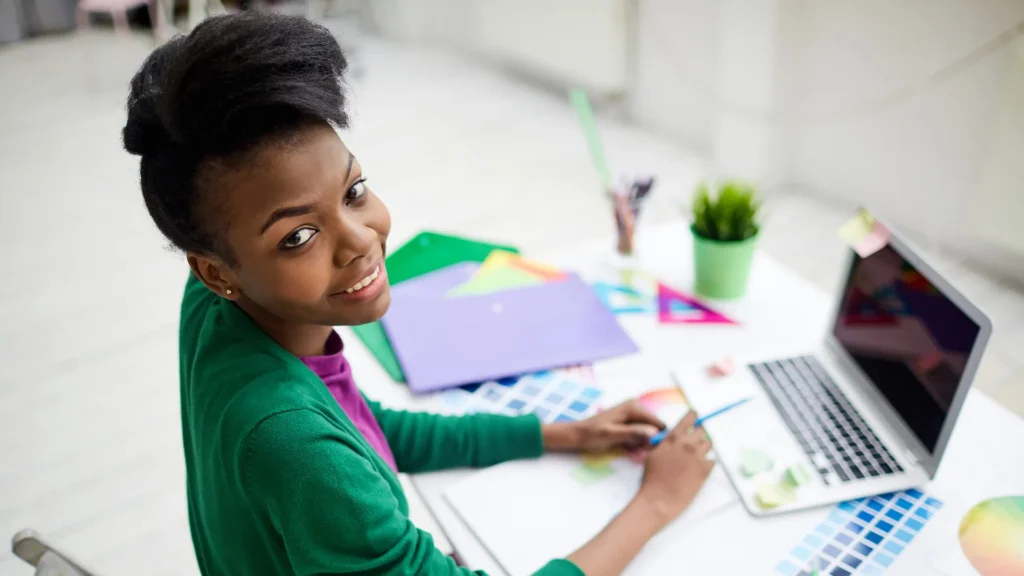 Young designer working on color palettes at her desk with a laptop and creative tools.