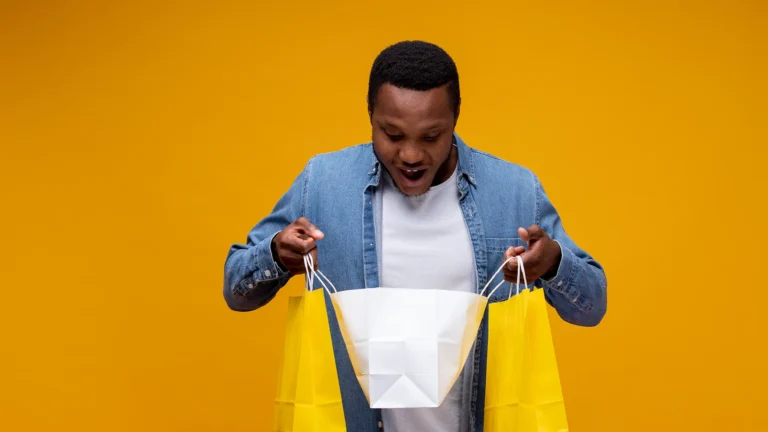 Excited man looking into shopping bags against a bright yellow background