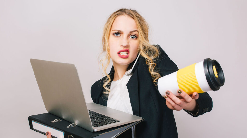 Overwhelmed businesswoman multitasking with laptop, folder, and coffee.