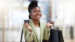 Smiling black woman holding a credit card and shopping bags in a mall symbolizing confident and empowered shopping