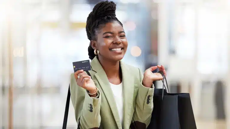 Smiling Black woman holding a credit card and shopping bags in a mall, symbolizing confident and empowered shopping.