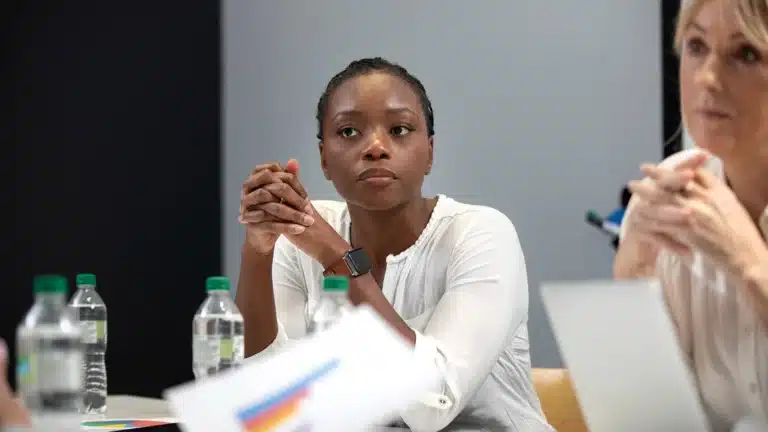 Businesswoman attentively listening in a meeting, seated at a table with charts, laptops, and water bottles.