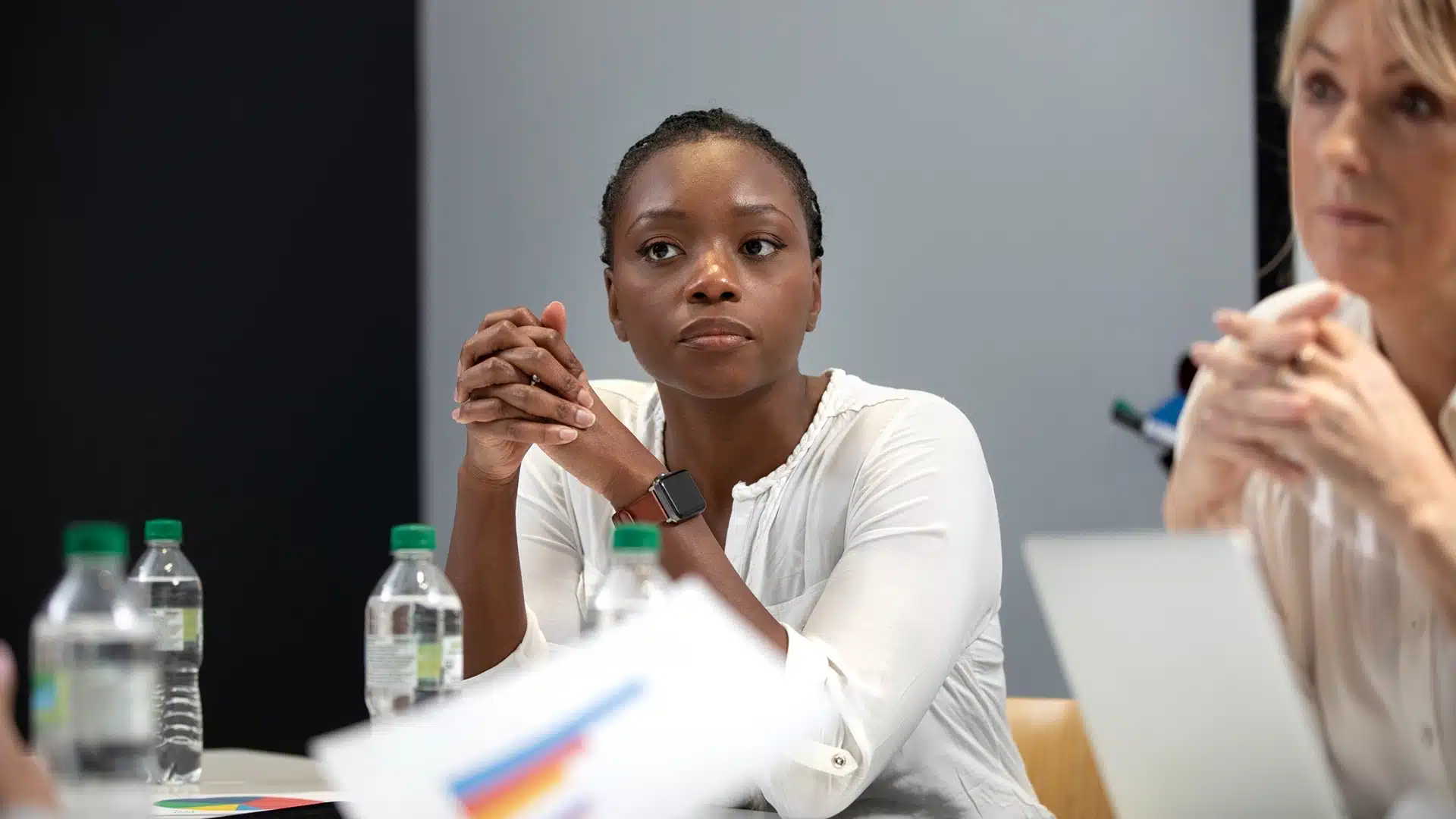 Businesswoman attentively listening in a meeting seated at a table with charts laptops and water bottles