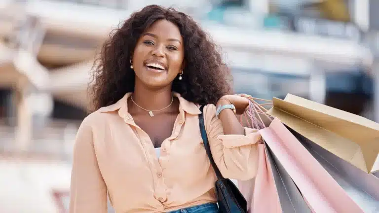 Smiling Black woman holding shopping bags outdoors after a successful shopping trip.