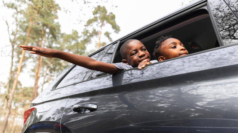Two happy african children leaning out of a car window smiling and enjoying the ride through a forested area
