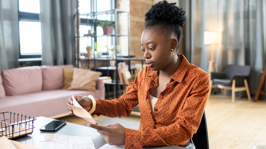 Young african woman in a home office placing a document into an envelope while reviewing papers