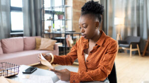 Young african woman in a home office placing a document into an envelope while reviewing papers