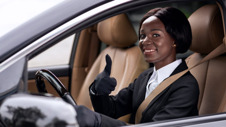 Smiling female taxi driver in uniform giving a thumbs up while seated in a car