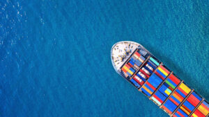 Top down aerial view of container ship sailing on clear blue water