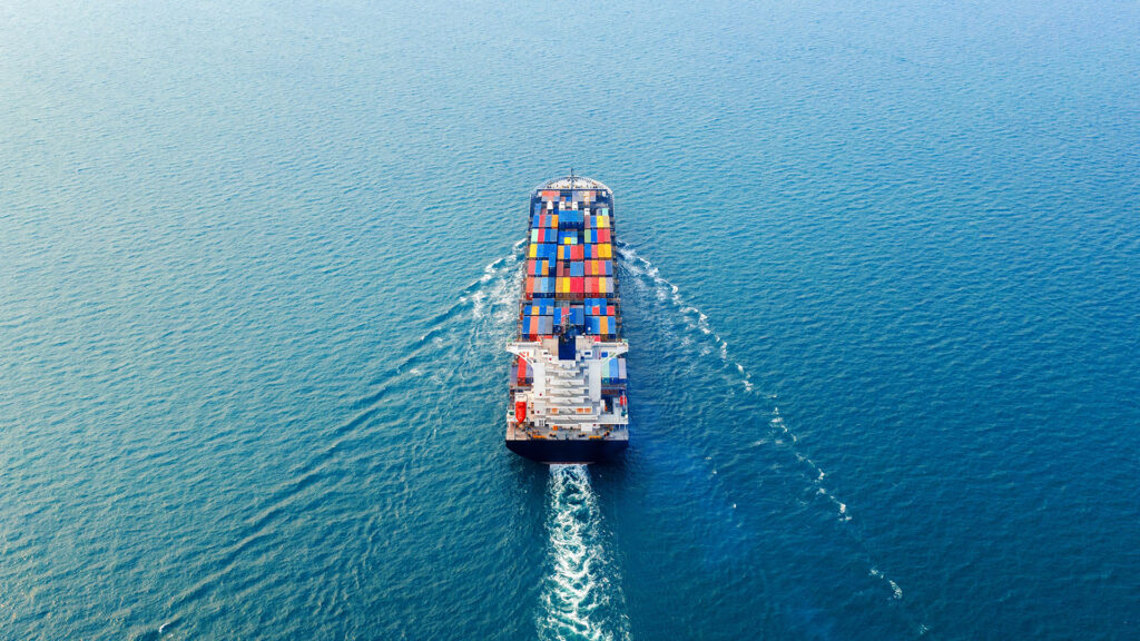 Aerial view of a cargo ship carrying colorful containers across the ocean.