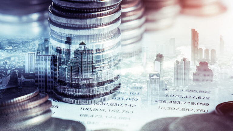 Overlay image of tall stacks of coins and a city skyline, symbolizing financial growth, investment, and economic development.