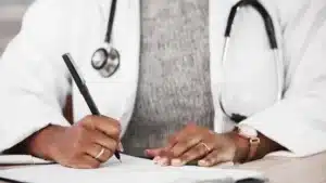 Doctor filling out medical documents with a stethoscope around their neck representing healthcare compliance and documentation practices