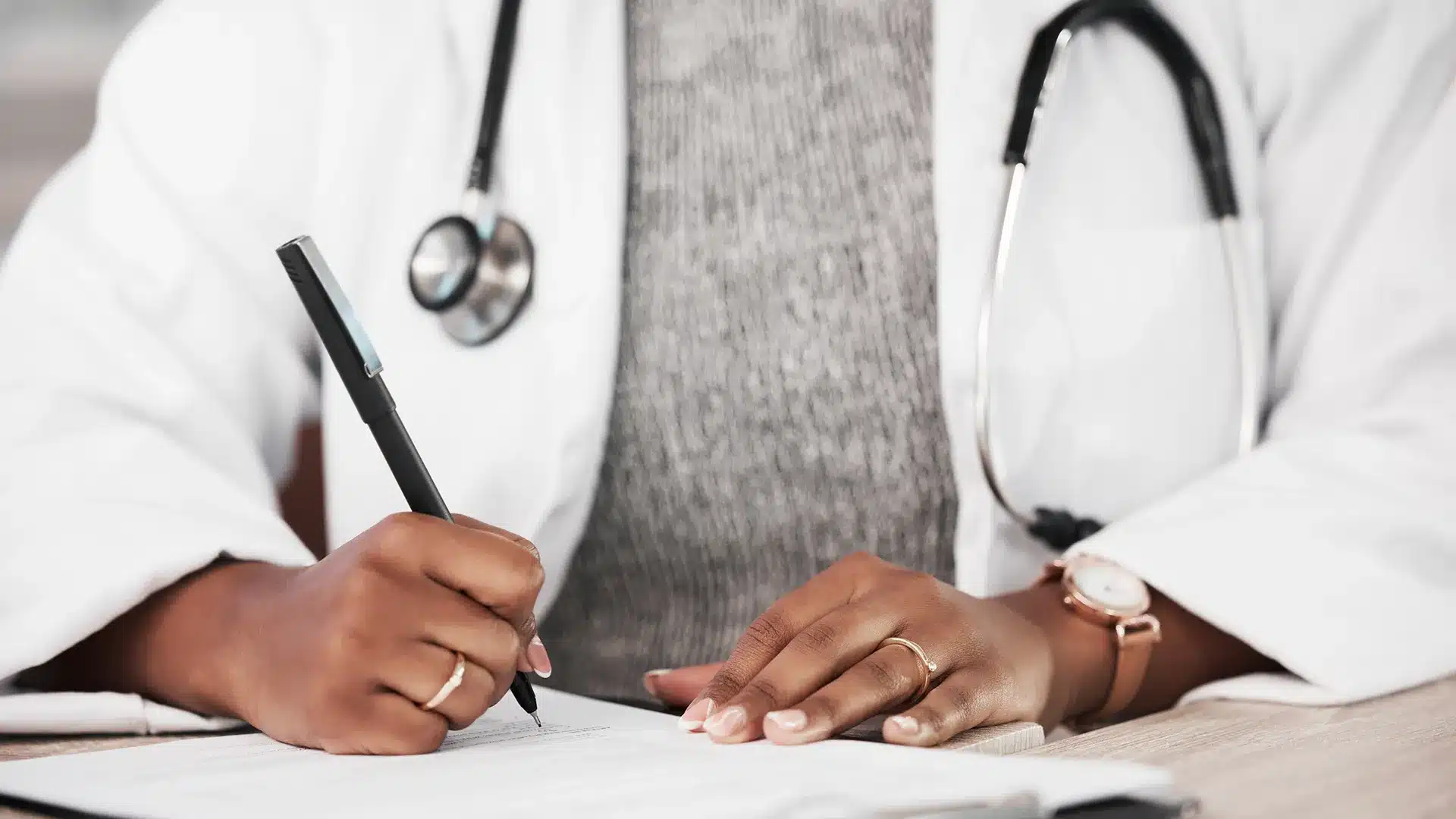 Doctor filling out medical documents with a stethoscope around their neck representing healthcare compliance and documentation practices